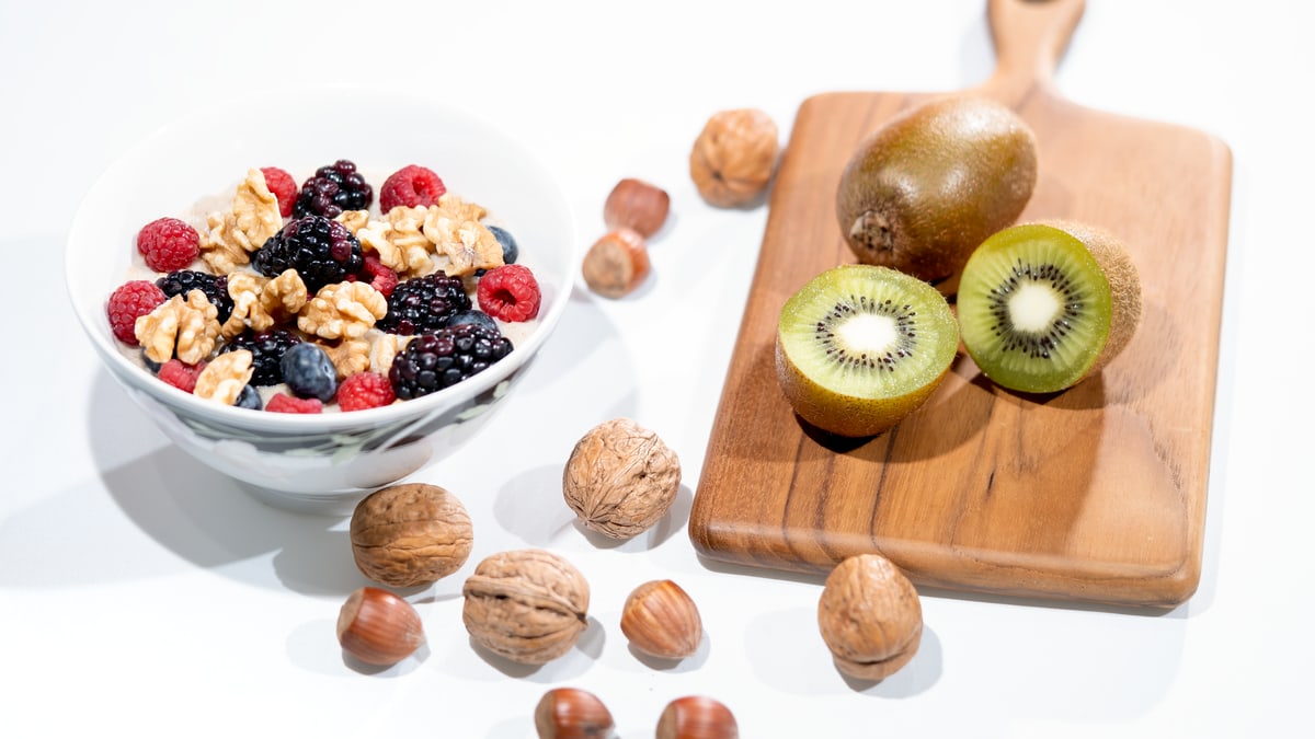 A vibrant bowl of mixed berries, walnuts, and kiwi on a cutting board. Perfect for a healthy breakfast.