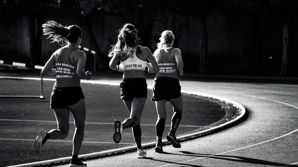 Black and white back view of unrecognizable fit female runners in sportswear running during track and field competition